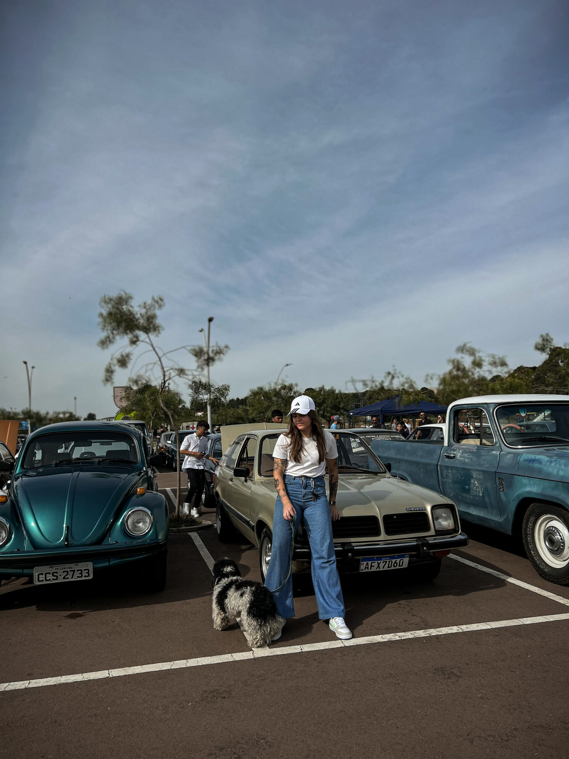 Kamila Lais Kuhn encostada em seu carro ao lado do seu cachorro, mostrando sua paixão por carros, liberdade e estilo de vida equilibrado.